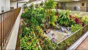 A multi-level indoor atrium with a central garden area featuring a small water feature and various tropical plants. - Ocean Front Condo at The Royal Sea-Cliff Resort (Kailua Kona)