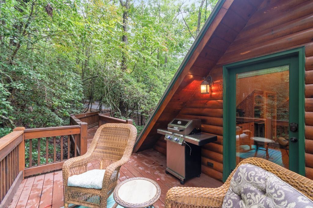 A log cabin with a deck featuring wicker furniture and a grill.