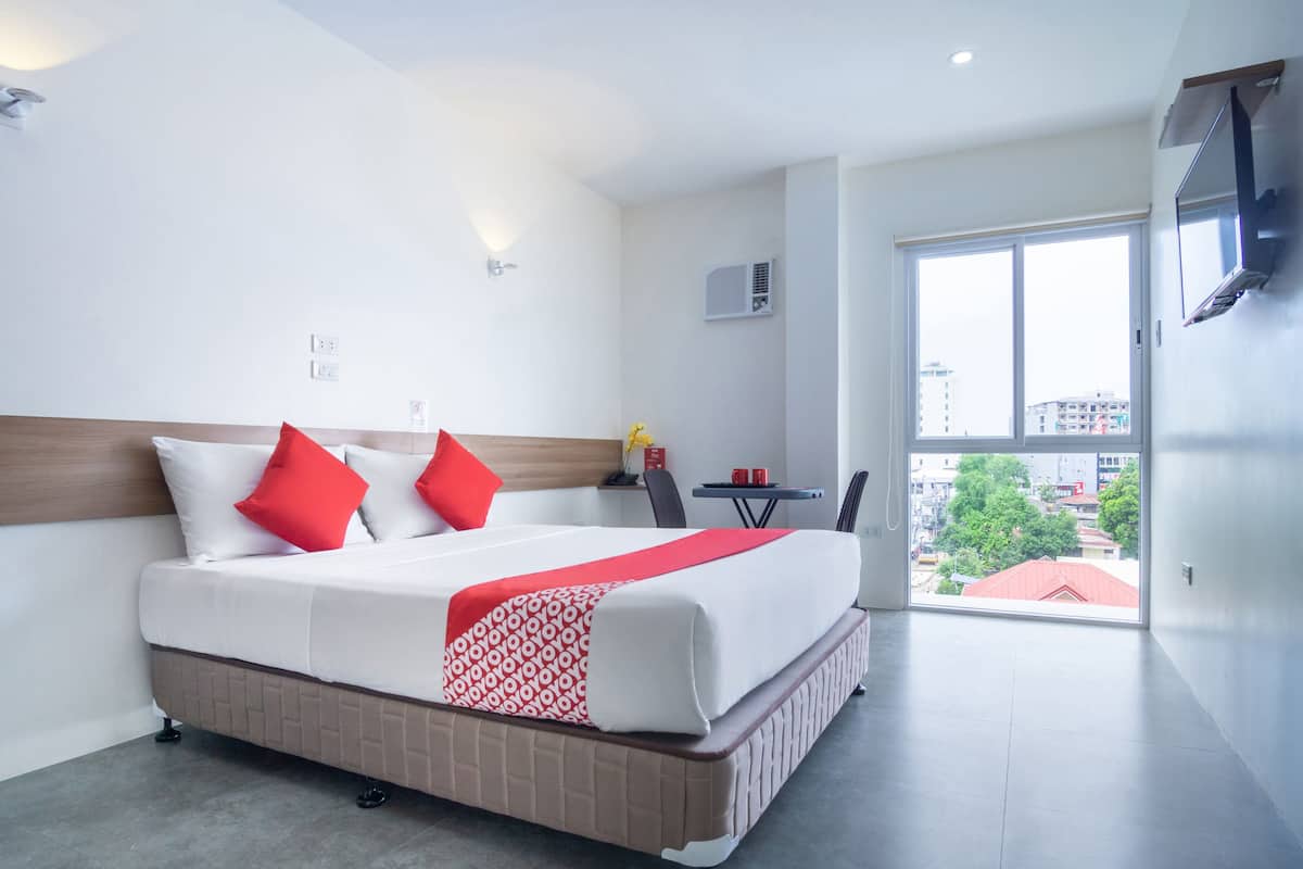 A hotel room with a large bed, a TV mounted on the wall, and a view of the city through the window.