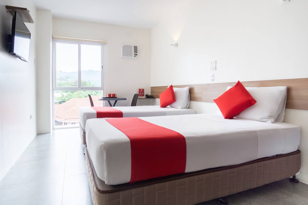 A hotel room with two beds, a TV, and a view of the outdoors.
