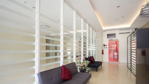 A modern lobby with a grey sofa, red cushions, a small table with a vase, and a red promotional banner. - 18 Suites Cebu (Cebu City)
