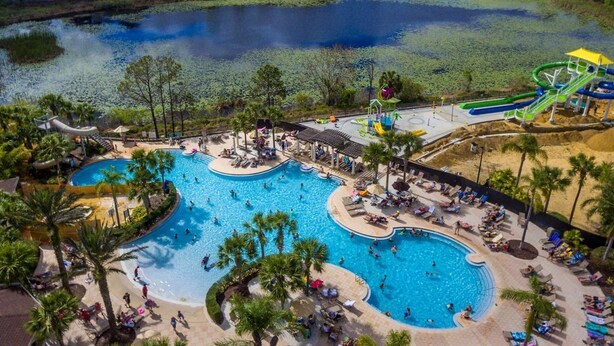 A resort with multiple swimming pools, a water park, and a view of a residential area in the background.