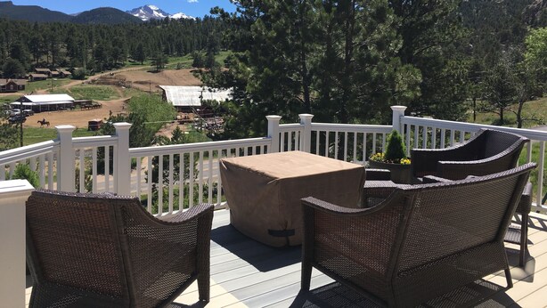 A deck with wicker furniture overlooking a scenic landscape with mountains and a clear sky.