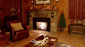 A cozy living room with a stone fireplace, a leather armchair, and a coffee table with antlers.