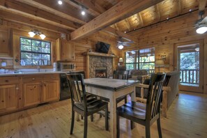 A wooden cabin interior with a stone fireplace, wooden dining table, and chairs. - A Tranquil Place | Pet Friendly | Fish From Cabin | Fire Pit | (Epworth)
