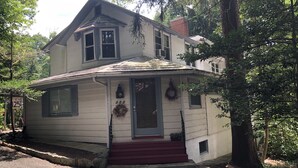A two-story house with a front porch, a mailbox, and a number sign.