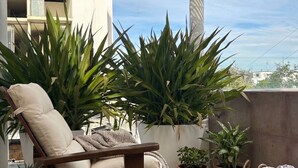 A cozy outdoor seating area with a wicker chair, a wooden table, and potted plants. - New Modern Condo, Private Pool, close to the Malecon & Marina Cortez La Paz BCS (La Paz, B.C.S.)
