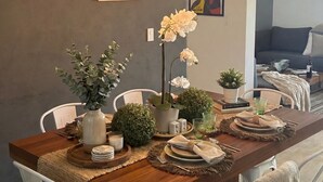 A modern dining area with a wooden table, white chairs, hanging pendant lights, and decorative plants. - New Modern Condo, Private Pool, close to the Malecon & Marina Cortez La Paz BCS (La Paz, B.C.S.)
