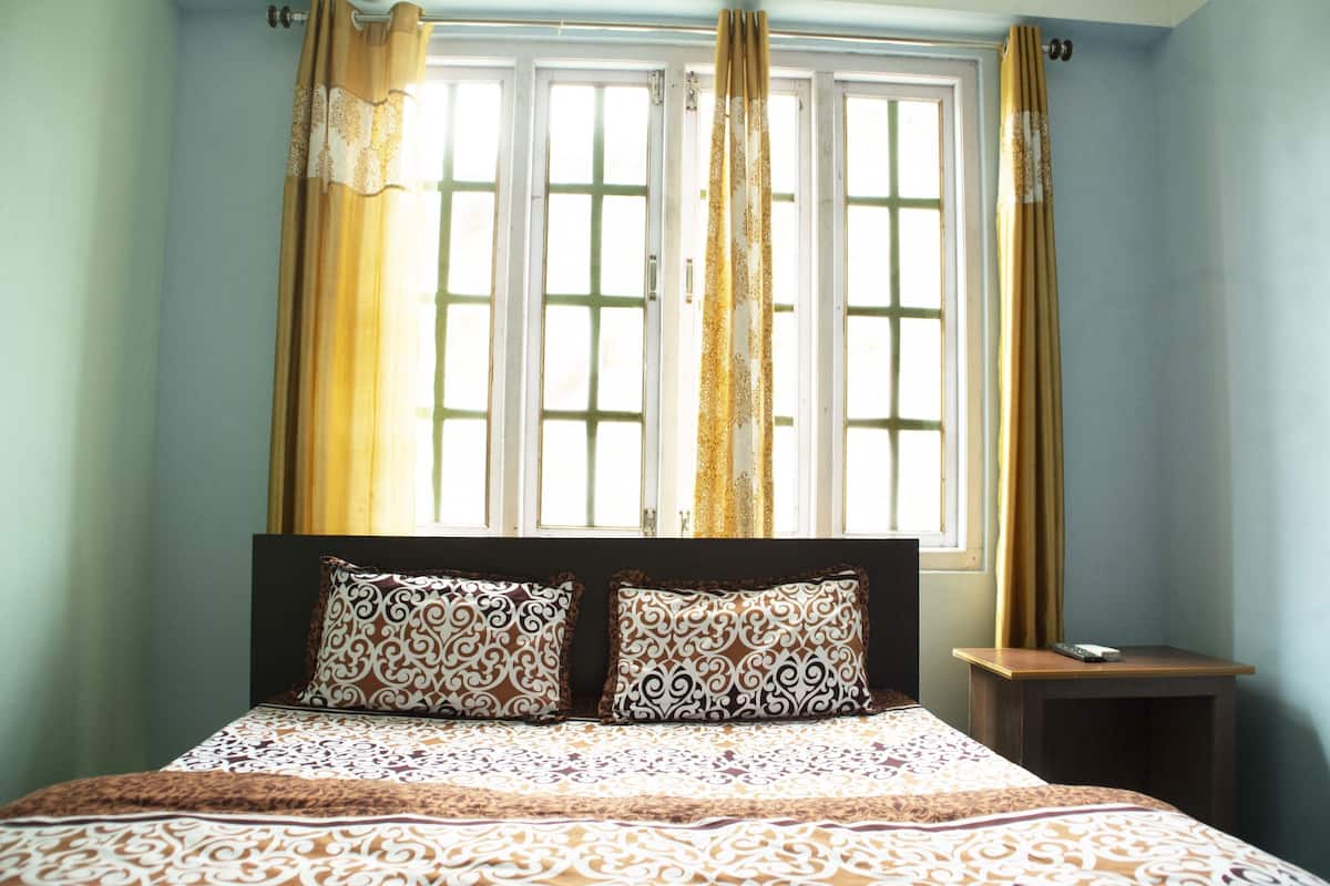 A bedroom with a bed, two patterned pillows, a nightstand, and a window with curtains.