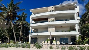Een meerlaags hotel met balkons, palmbomen en een zandstrand op de voorgrond.