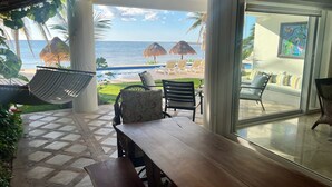 Een terras met een houten tafel en stoelen, een hangmat, en uitzicht op zee en strand.