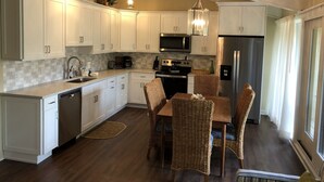 A modern kitchen with white cabinets, a stainless steel refrigerator, a microwave, and a dining area with wicker chairs. - 3 Bedroom, 3 Bath Oceanside Beach Villa (Hilton Head Island)