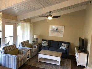 Uma sala de estar com sofás listrados, uma mesa de centro, um ventilador de teto, um quadro e uma TV em um móvel.