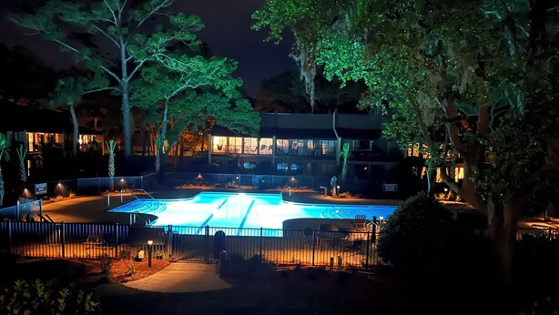 A nighttime view of a swimming pool area with surrounding trees and a building with illuminated windows. - 3 Bedroom, 3 Bath Oceanside Beach Villa (Hilton Head Island)