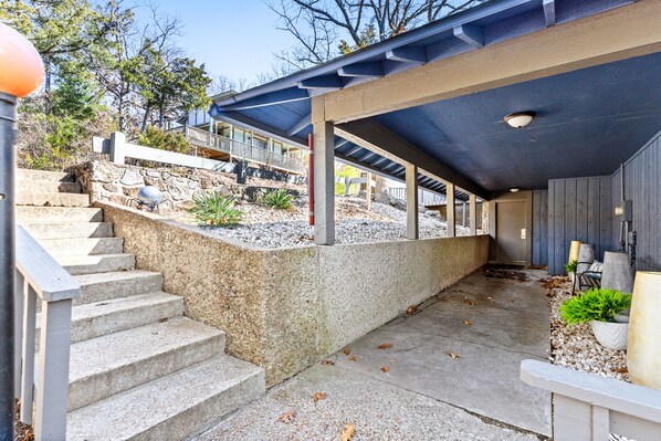 A covered outdoor area with concrete steps leading up to a stone wall, a wooden deck, and a door leading to a building.