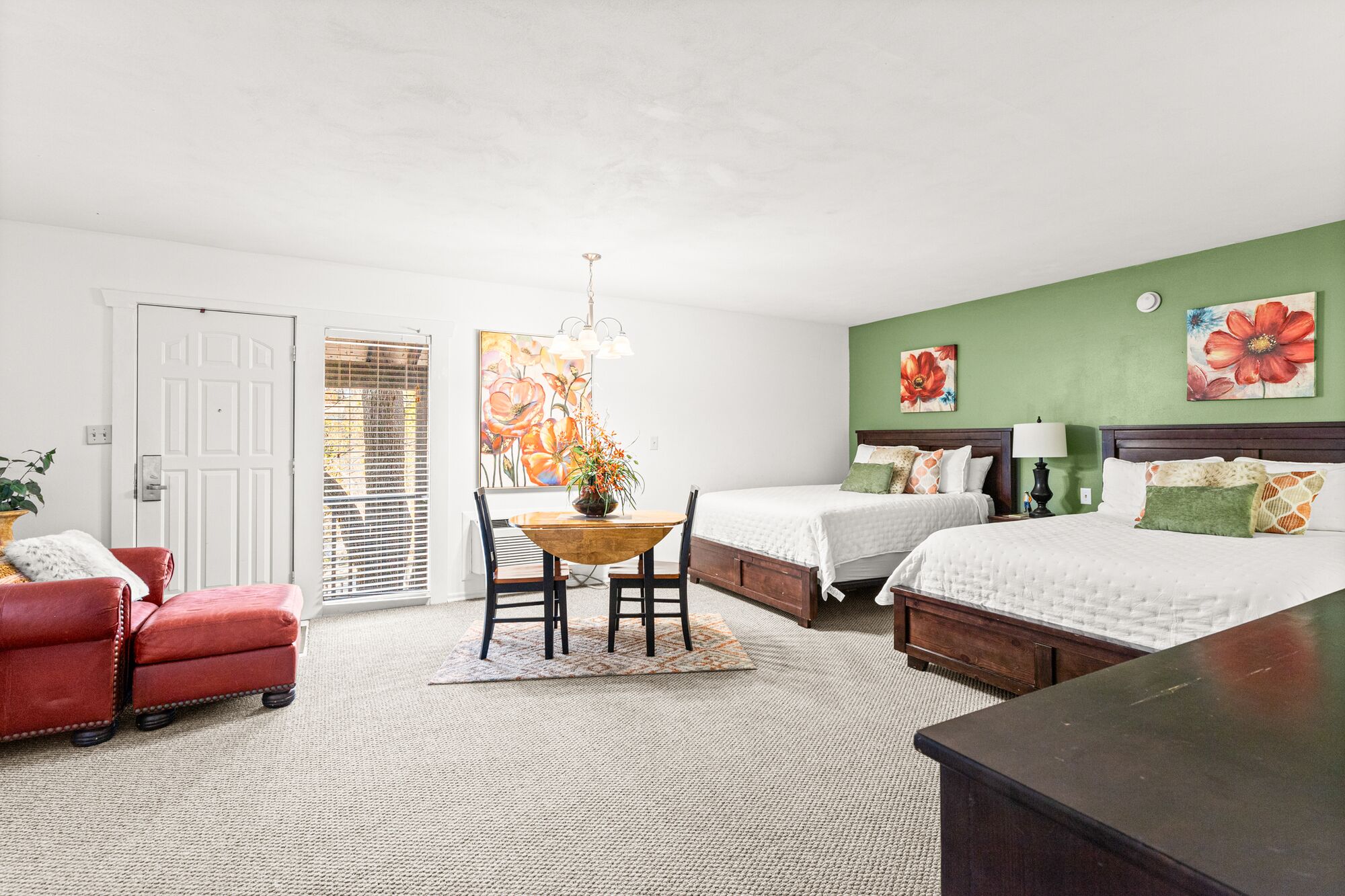 A hotel room with two beds, a dining table, and a red armchair.