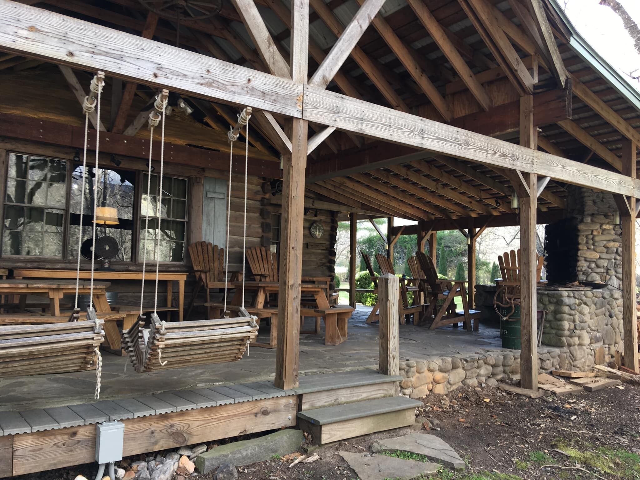 A rustic wooden cabin with a stone fireplace, wooden benches, and a covered porch area.