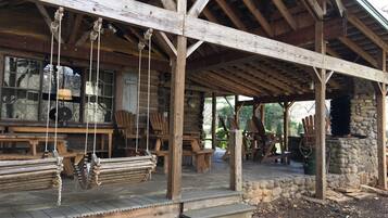 A rustic wooden cabin with a stone fireplace, wooden benches, and a covered porch area.