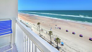 Un balcone con vista su una spiaggia, con spiaggia sabbiosa, onde dell'oceano e diversi ombrelloni.