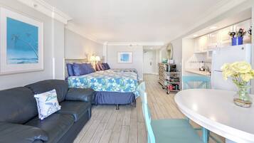 Ein kompaktes Hotelzimmer mit Bett, einer Schlafcouch, einem Esstisch und einer Küchenzeile.
