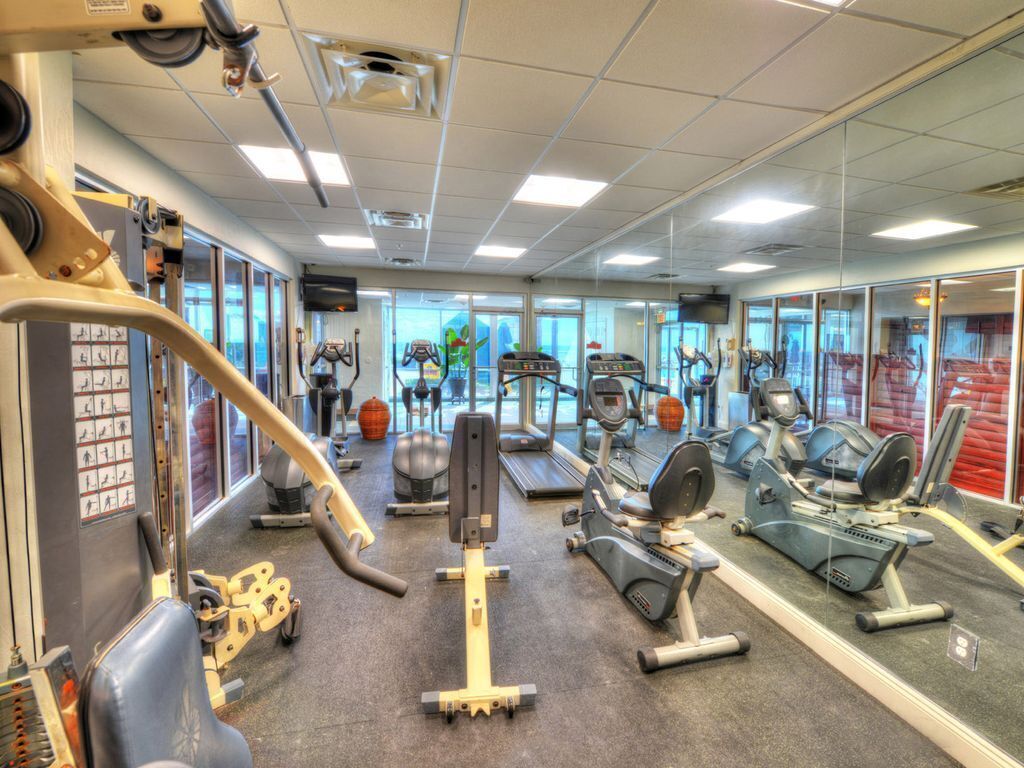 A gym with various exercise machines, mirrors, and a large window.