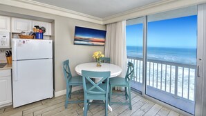 Cucina con frigorifero, tavolo da pranzo con sedie e vista sull'oceano tramite una porta scorrevole in vetro.