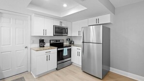 A modern kitchen with white cabinets, a stainless steel refrigerator, a microwave, and a coffee maker. - Cozy Beach House ( Walking Distance to Beach) (New Smyrna Beach)