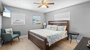 A bedroom with a bed, a ceiling fan, a TV, and a chair. - Cozy Beach House ( Walking Distance to Beach) (New Smyrna Beach)