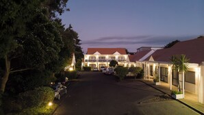 A hotel with a central building and two wings, featuring a red roof, multiple balconies, and a parking area with cars. - Mt. Wellington Motel (Auckland)