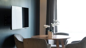 A modern room with a flat-screen TV mounted on the wall, a round wooden table with chairs, and a potted orchid plant. - Mt. Wellington Motel (Auckland)