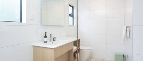 Et moderne badeværelse med hvid vask, spejl og toilet.