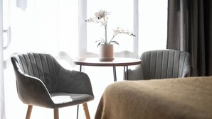 A hotel room with two grey upholstered chairs, a round table with a potted orchid, and a large window with curtains. - Mt. Wellington Motel (Auckland)