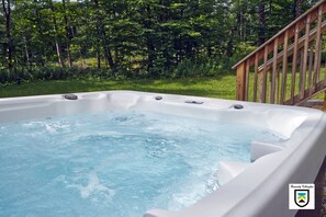 A hot tub with a wooden deck and a forested background.