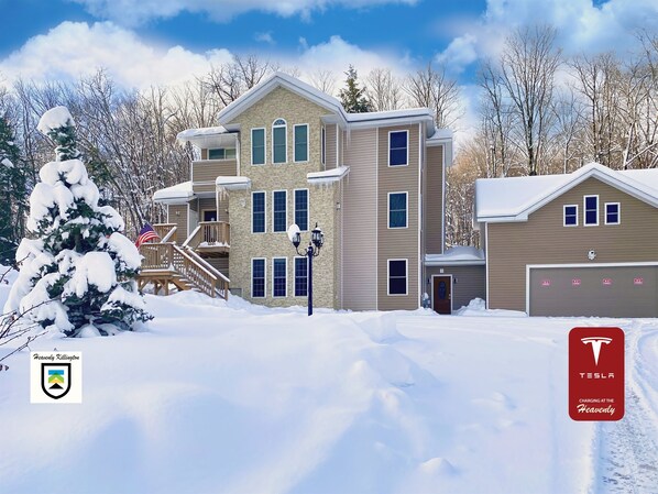 A multi-story residential building with a snow-covered landscape, a visible American flag, and a Tesla logo indicating charging availability.