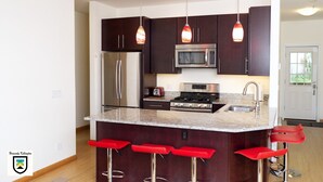A modern kitchen with dark wood cabinets, stainless steel appliances, and a central island with red bar stools.