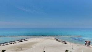 Una playa con aguas azul cristalina, orilla de arena y varias sombrillas.