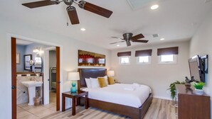 A hotel room with a large bed, two bedside tables, a ceiling fan, a TV, and a bathroom with a sink and mirror. - Seascape Family Beach Home Getaway! Steps to Sand (San Diego)