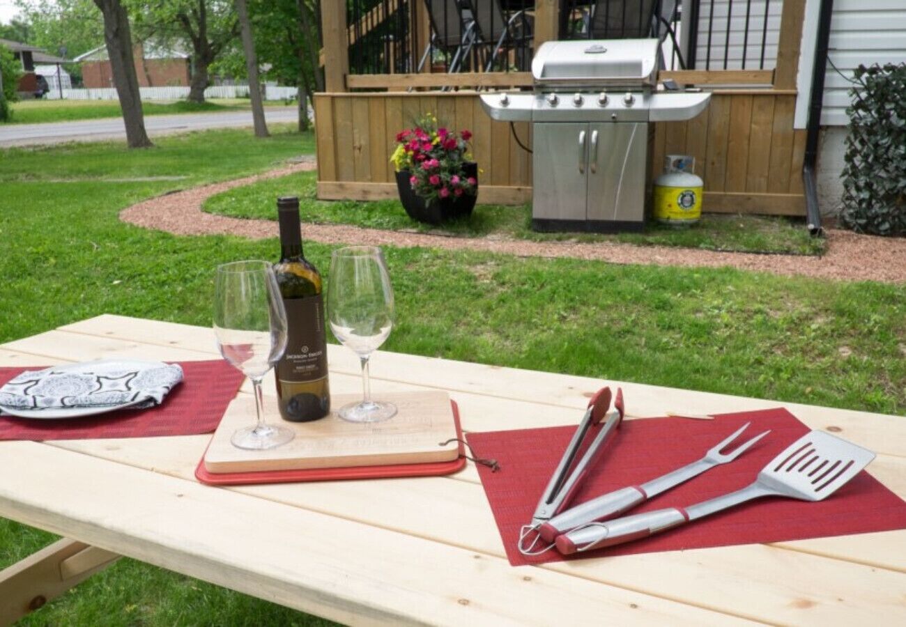 A picnic setup with a bottle of wine, two glasses, a notebook, and barbecue utensils on a wooden table.
