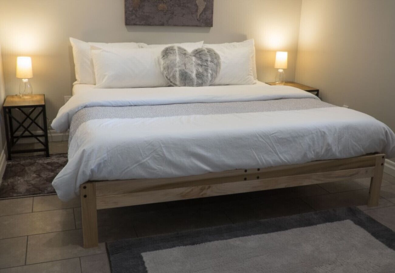 A bed with a wooden frame, white bedding, and a heart-shaped pillow. There are two bedside tables with lamps.