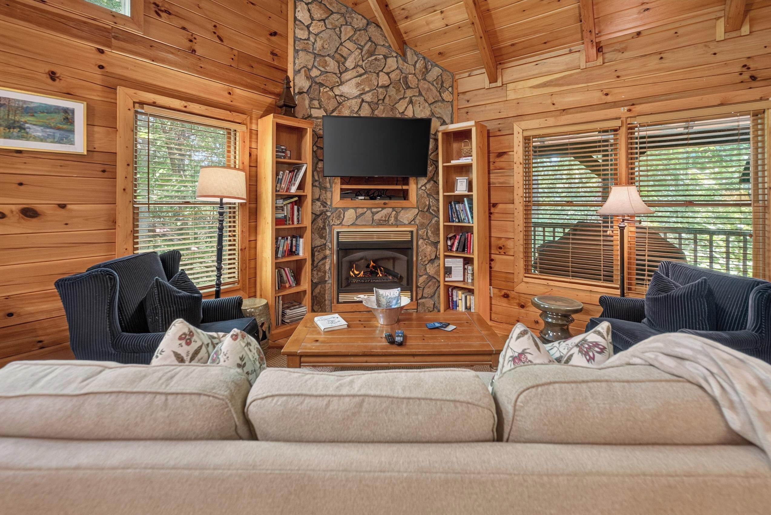 A cozy living room with a stone fireplace, wooden walls, and a flat-screen TV mounted above it.