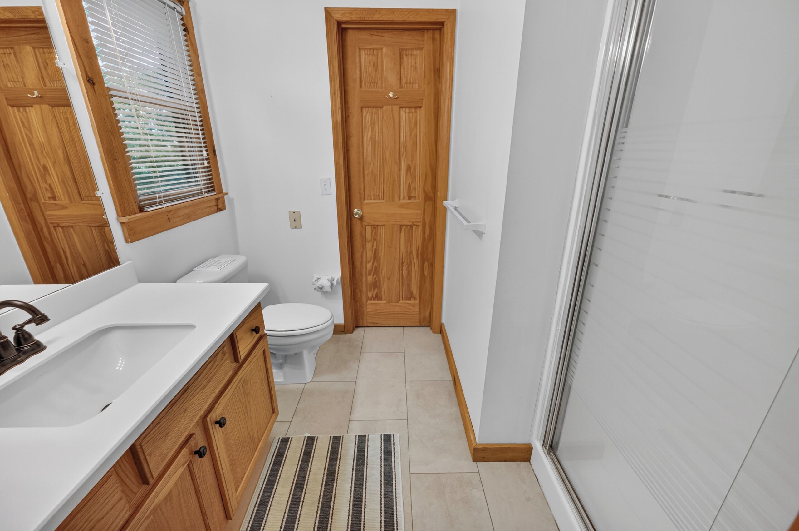 A bathroom with a white sink, wooden cabinets, a toilet, and a shower area.