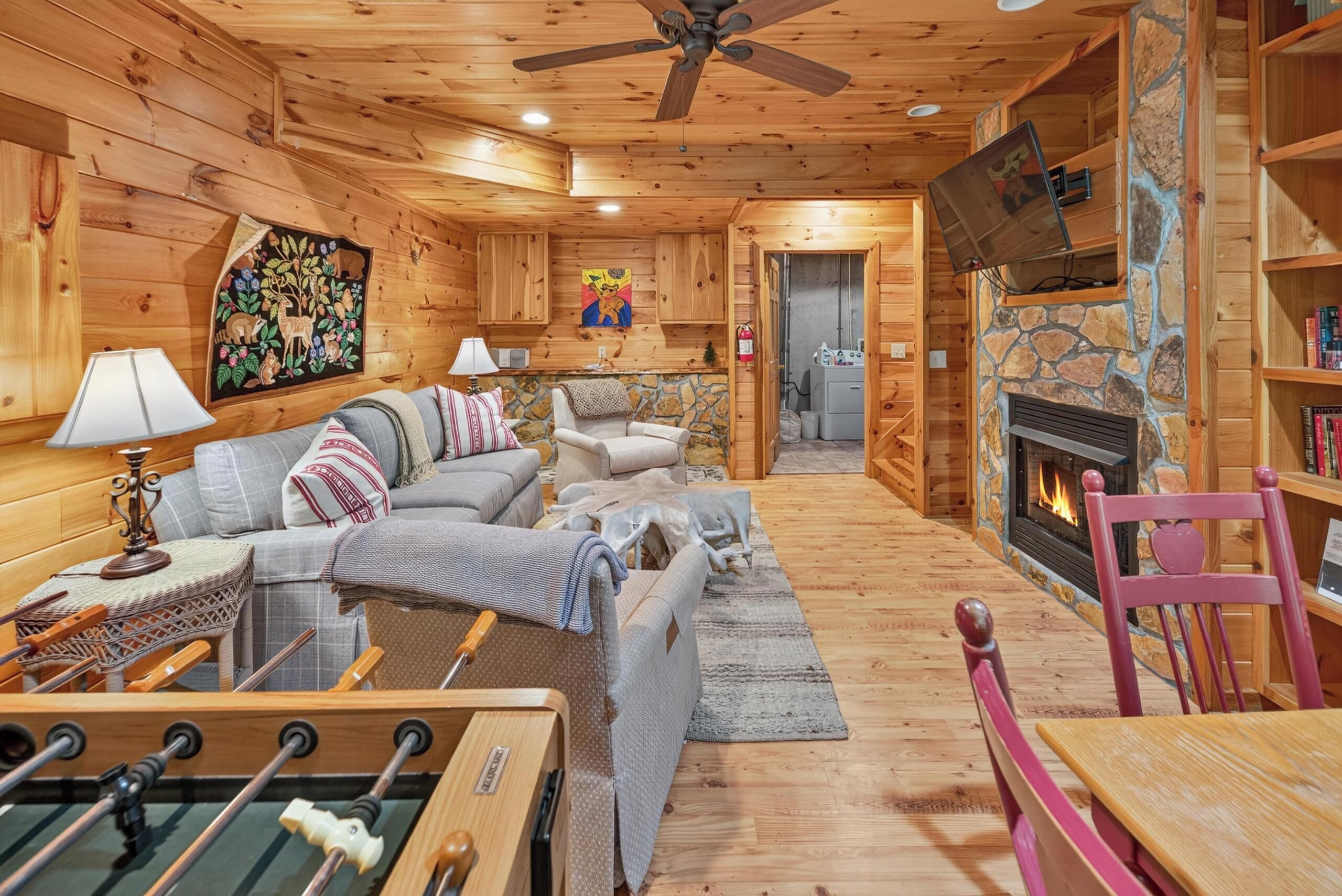 A cozy cabin interior with a living room, a fireplace, and a game table.