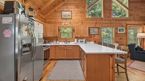 A wooden cabin kitchen with a refrigerator, stove, microwave, and wooden cabinets. - Dancing Bears | Hot Tub | Grill (Morganton)