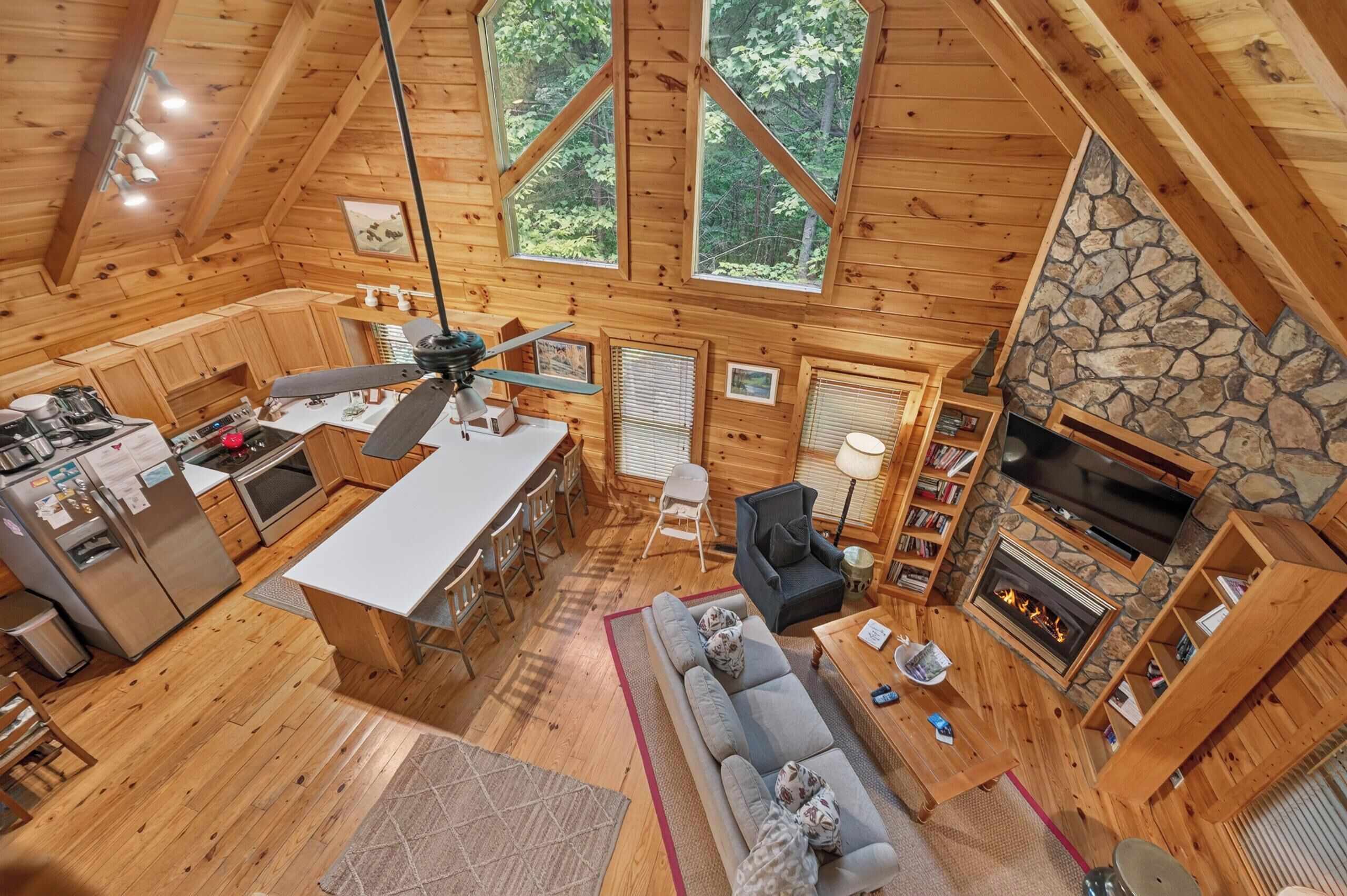 A spacious cabin with a kitchen, dining area, and living room, featuring wooden walls, a stone fireplace, and large windows.