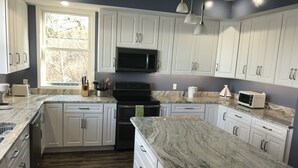 A modern kitchen with white cabinets, a large island, and a built-in microwave.