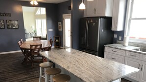 A modern kitchen with a marble countertop, a black refrigerator, and a dining area with a wooden table and bar stools.