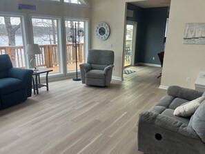 A living room with a blue armchair, a grey armchair, a small table with a lamp, and a clock on the wall. - Blue Heron Lodge Lake Gaston, Sleeps 20, Private Dock & Sundeck, Family-Friendly (Littleton)