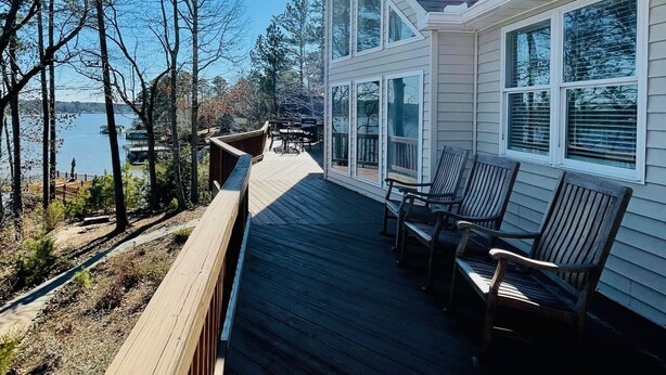 A wooden deck with outdoor seating, overlooking a body of water and trees.