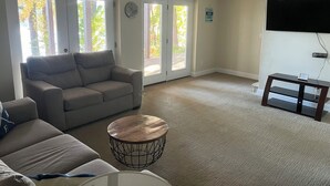 A living room with a sofa, a coffee table, and a TV mounted on the wall.