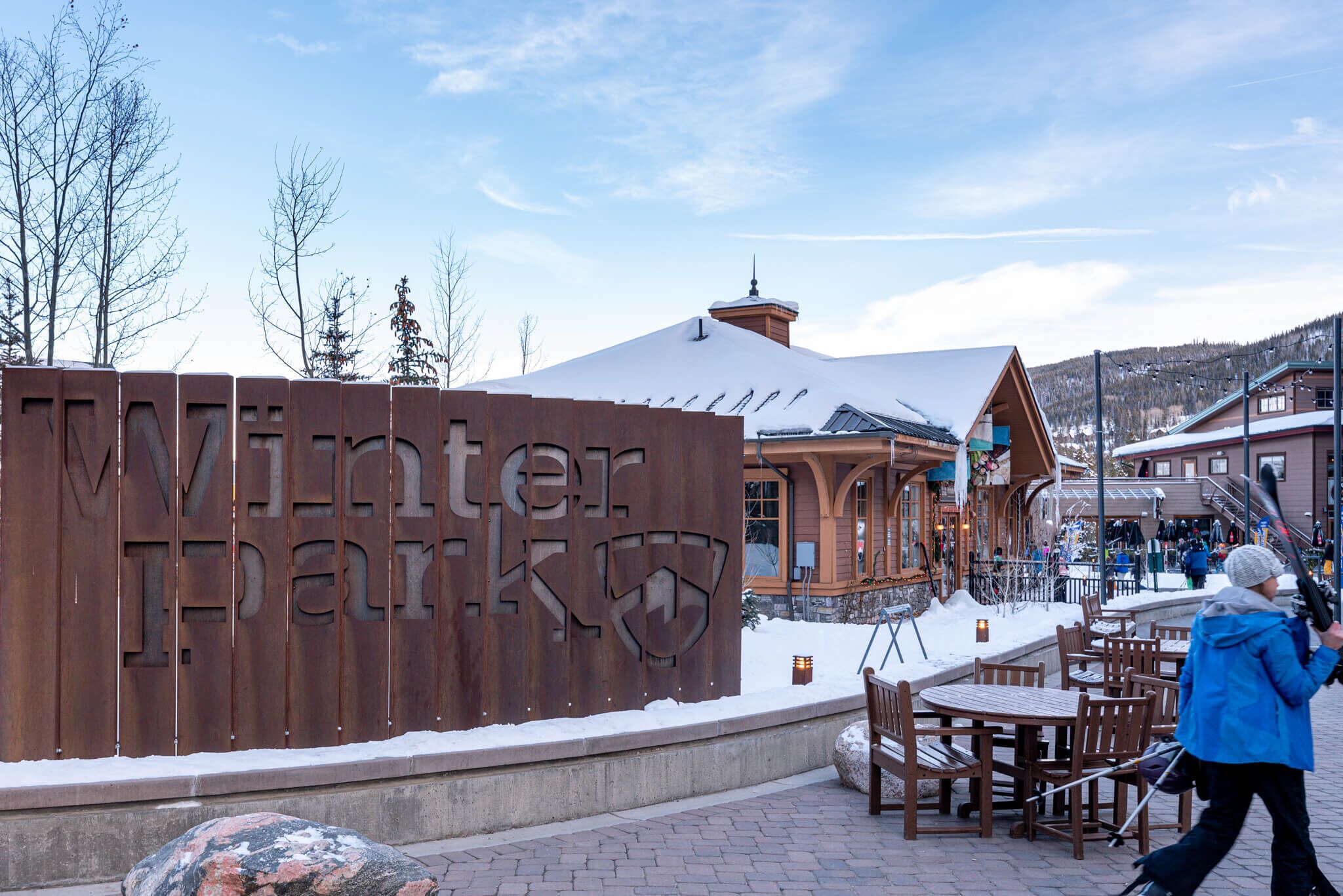 A wooden sign with "Winter Parks" carved into it, a building with a sloped roof, and outdoor seating.